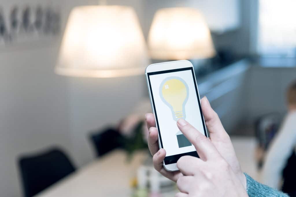 A hand holds a phone up in front of smart lighting hanging from the ceiling.