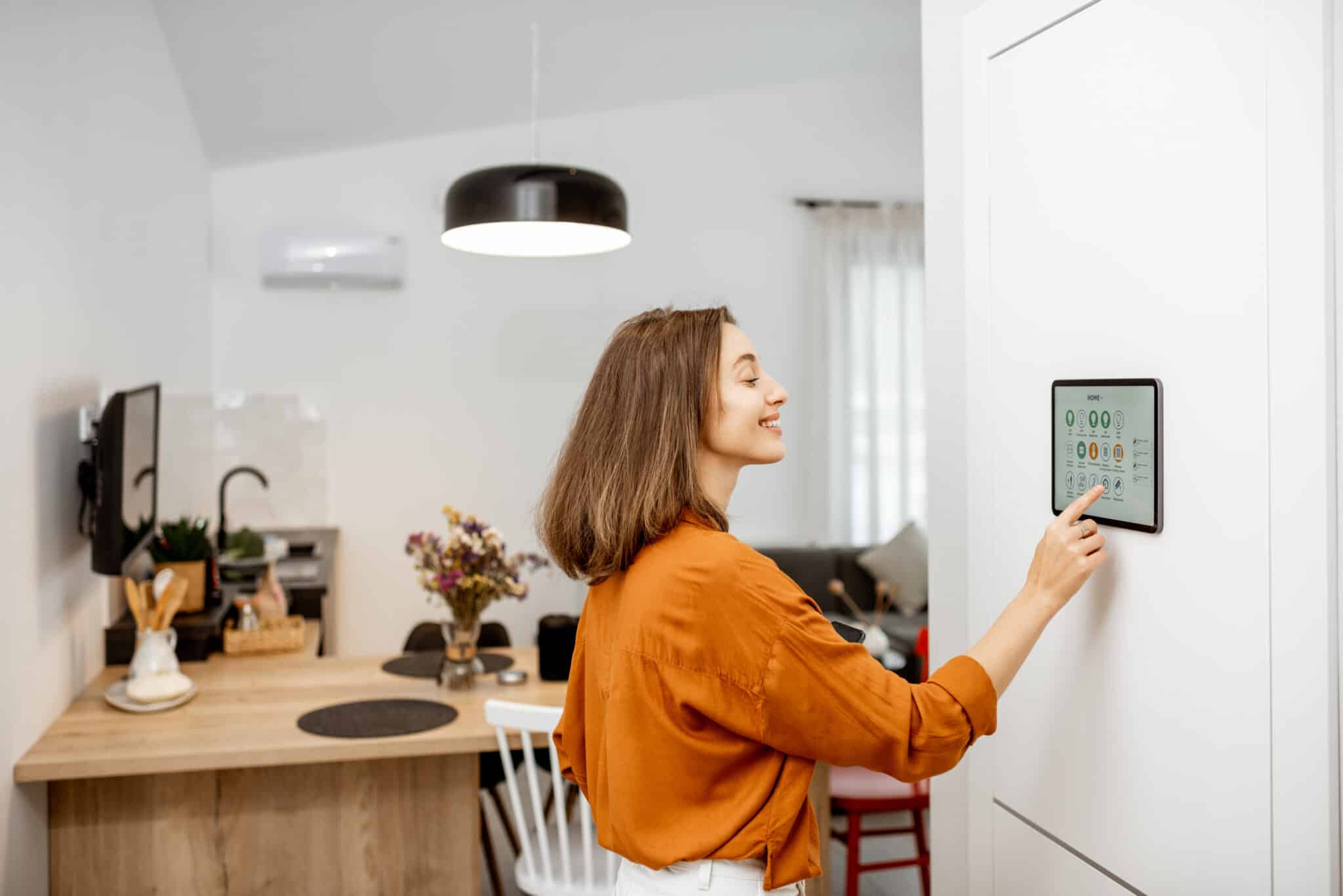 A woman controls her home using a smart lighting digital touch screen panel installed on the wall in the living room.