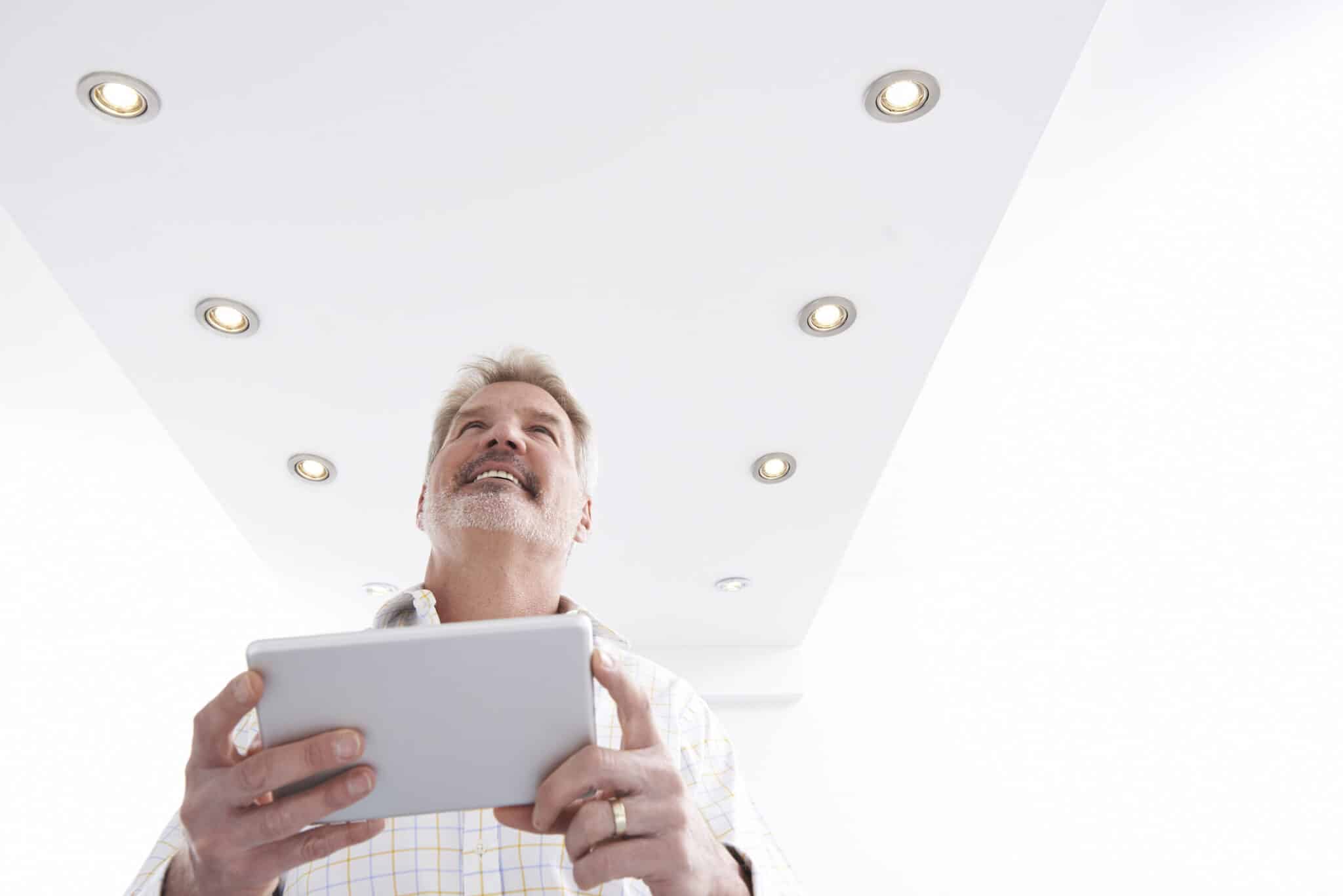 Man Controlling Lighting With App On Digital Tablet, Indoor Lighting Trends.